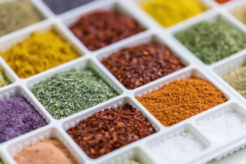 White plastic tray with multiple compartments filled with colorful spices arranged in a grid pattern