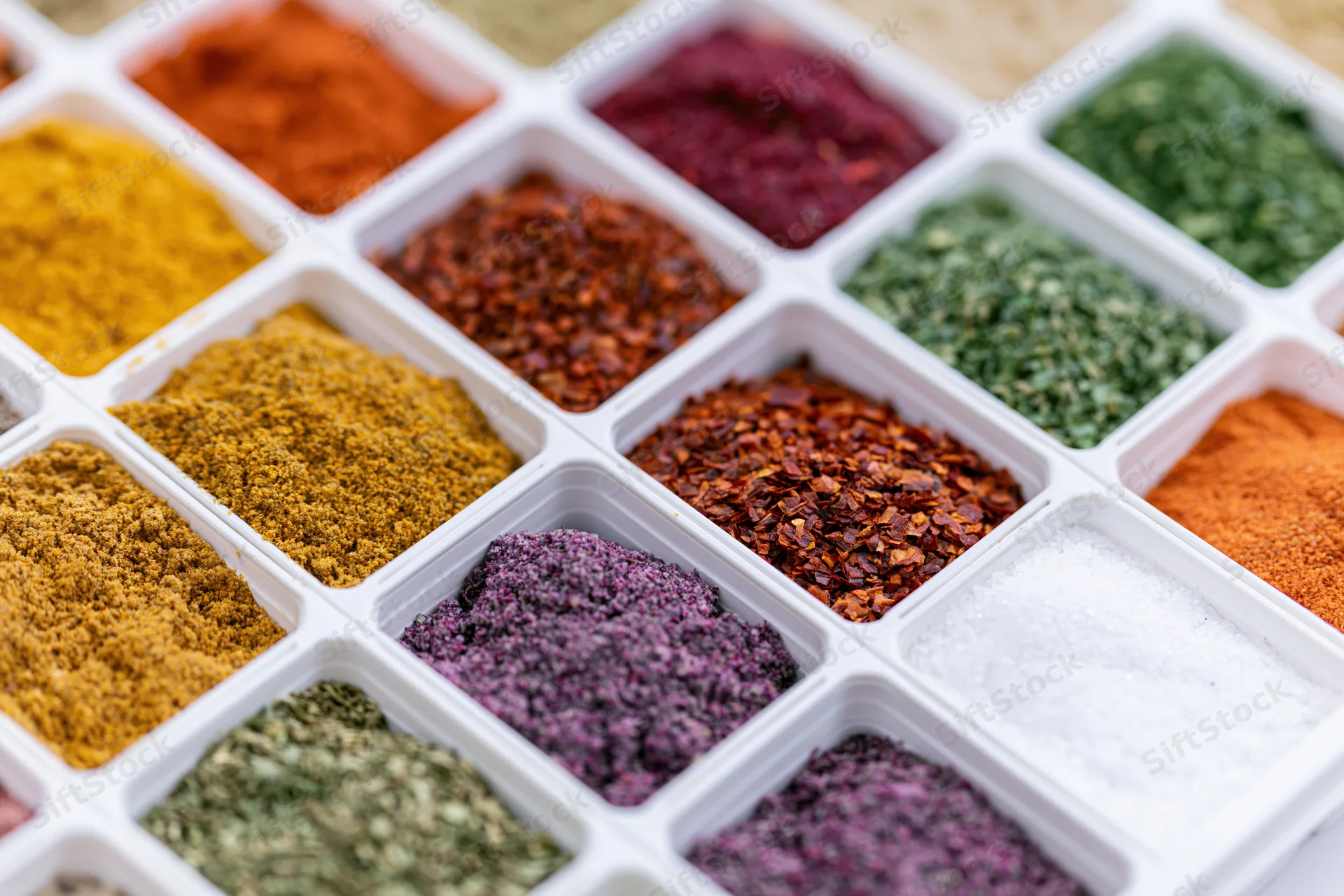 Colorful spices arranged in a white plastic grid tray for culinary use