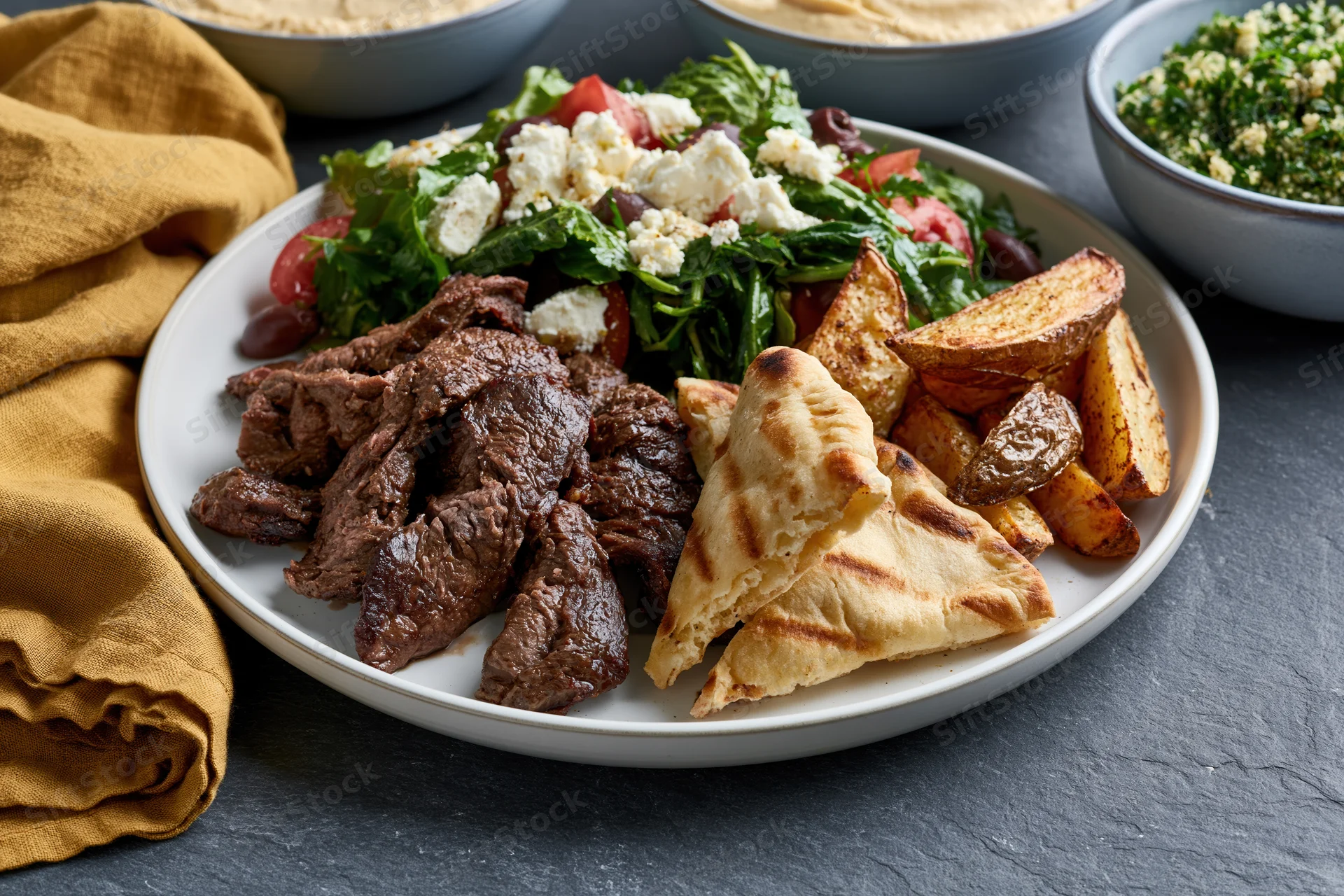 Plate of shawarma beef with grilled pita wedges and salad on a stone table