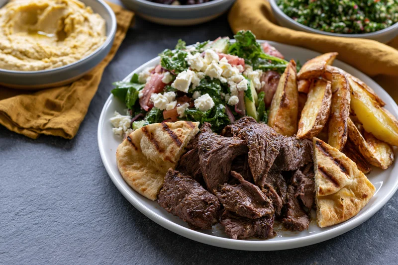 Plate of shawarma beef with grilled pita wedges and salad on dark surface