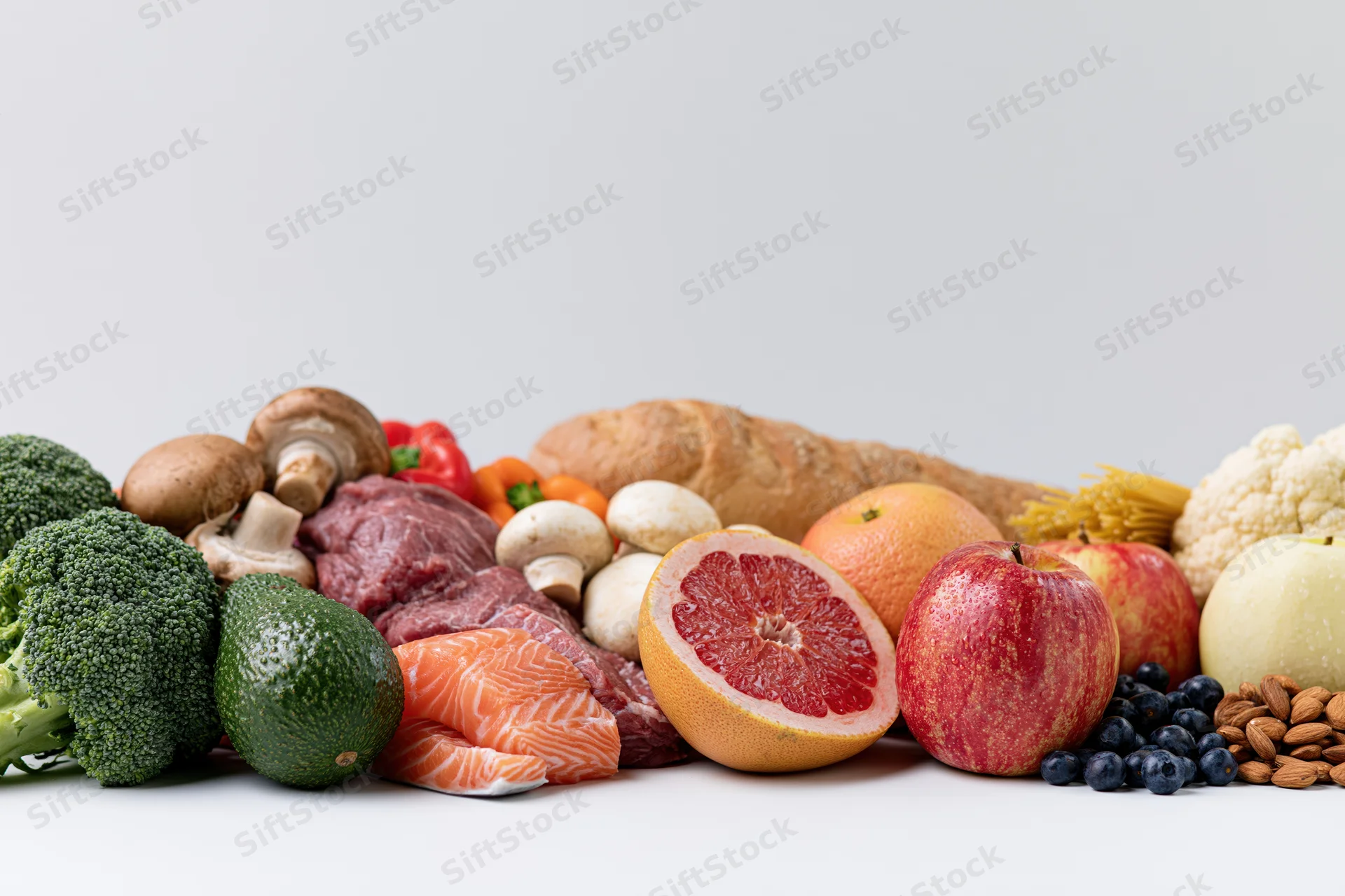 Variety of raw whole foods arranged in a low horizontal spread on white surface