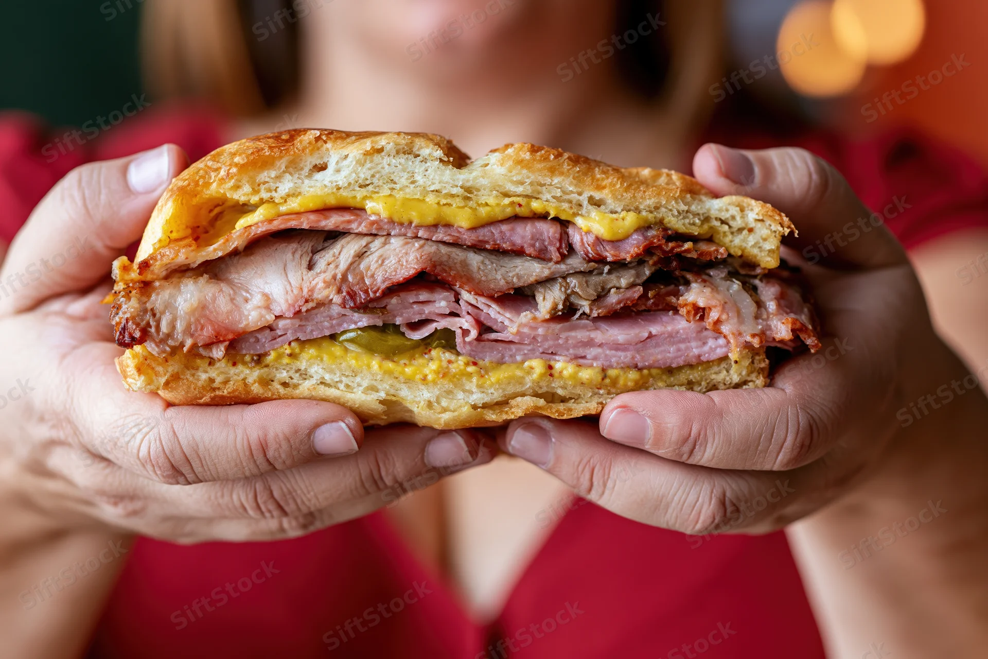 Woman holding thick cuban sandwich with layers of ham, pork, cheese and mustard