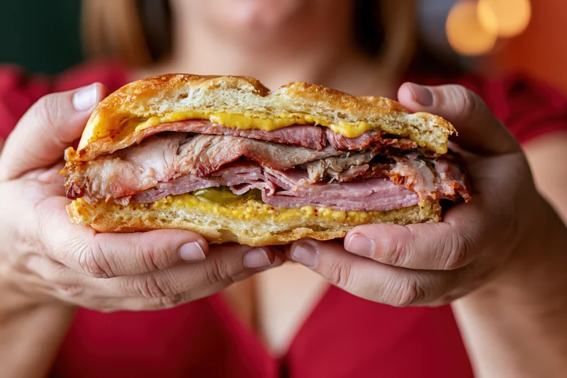 Woman holding thick cuban sandwich with layers of ham, pork, cheese and mustard