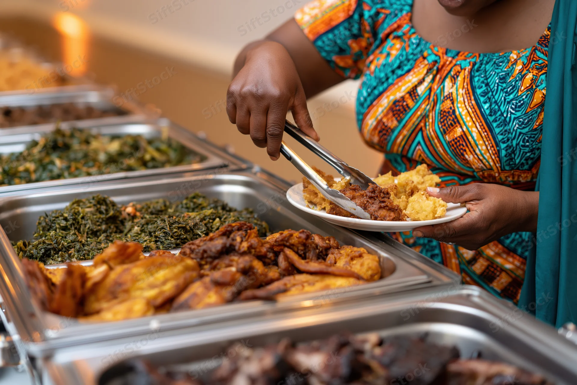Woman in colorful african print dress serving food from buffet line with tongs and plate