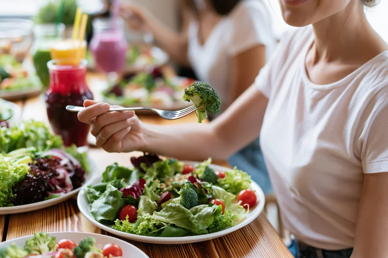 Woman eating fresh garden salad with broccoli on fork at wooden table