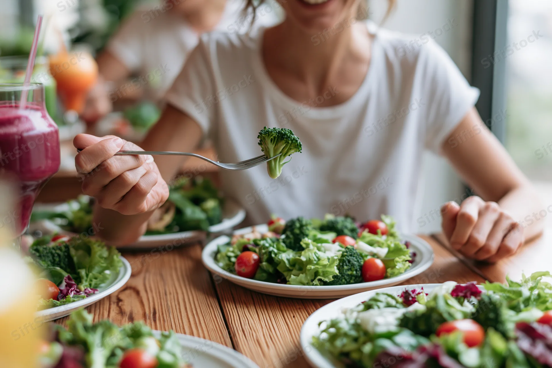 Woman eating fresh garden salad with broccoli and tomatoes at wooden dining table