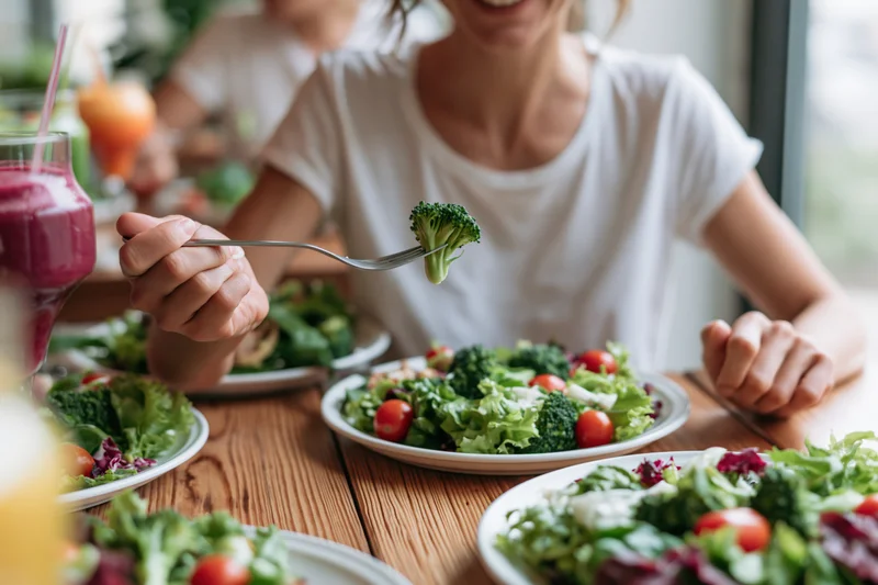Woman eating fresh garden salad with broccoli and tomatoes at wooden dining table
