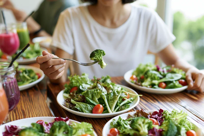 Woman eating fresh garden salad with broccoli and tomatoes at wooden dining table