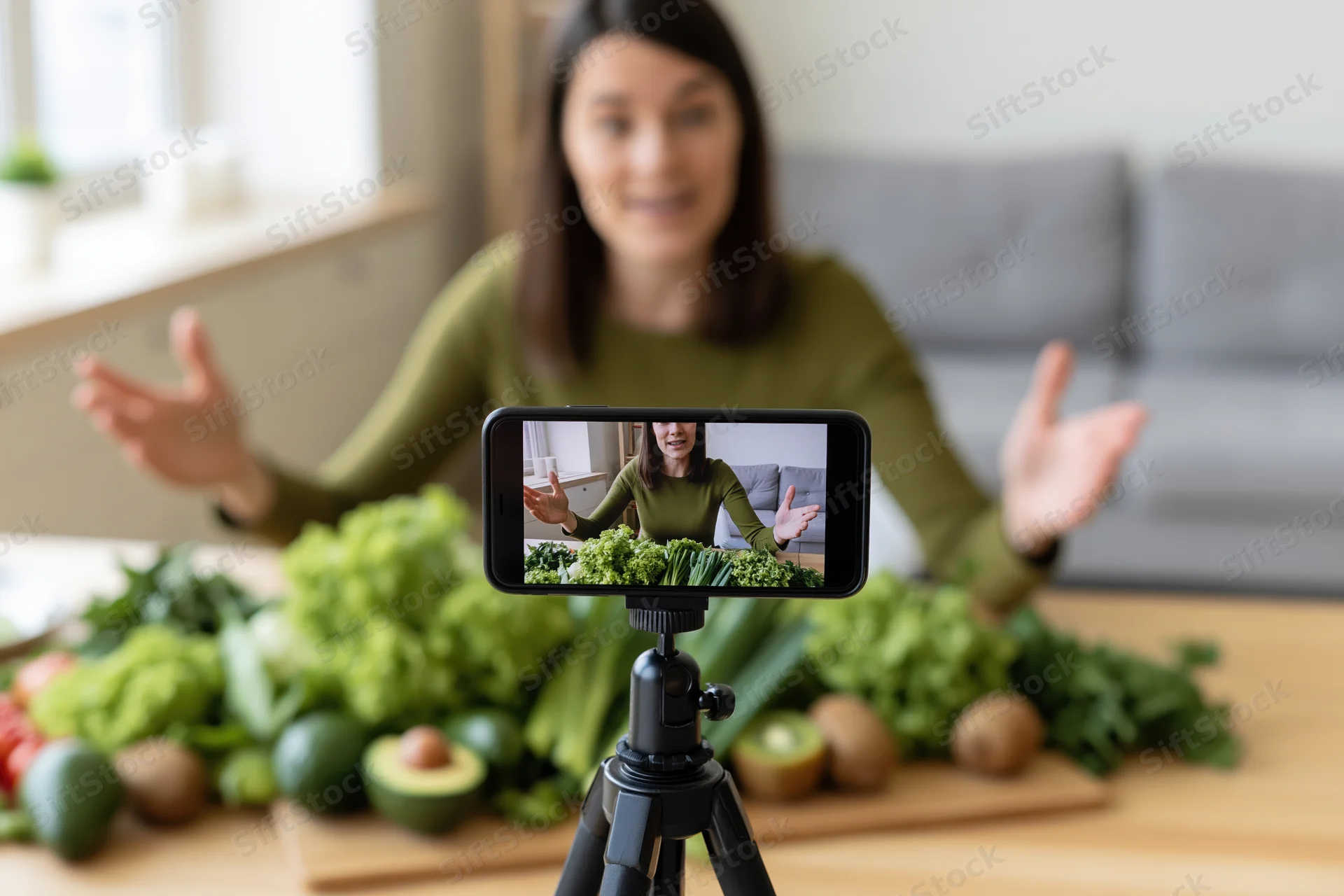 Woman recording video tutorial with vegetables on table in kitchen
