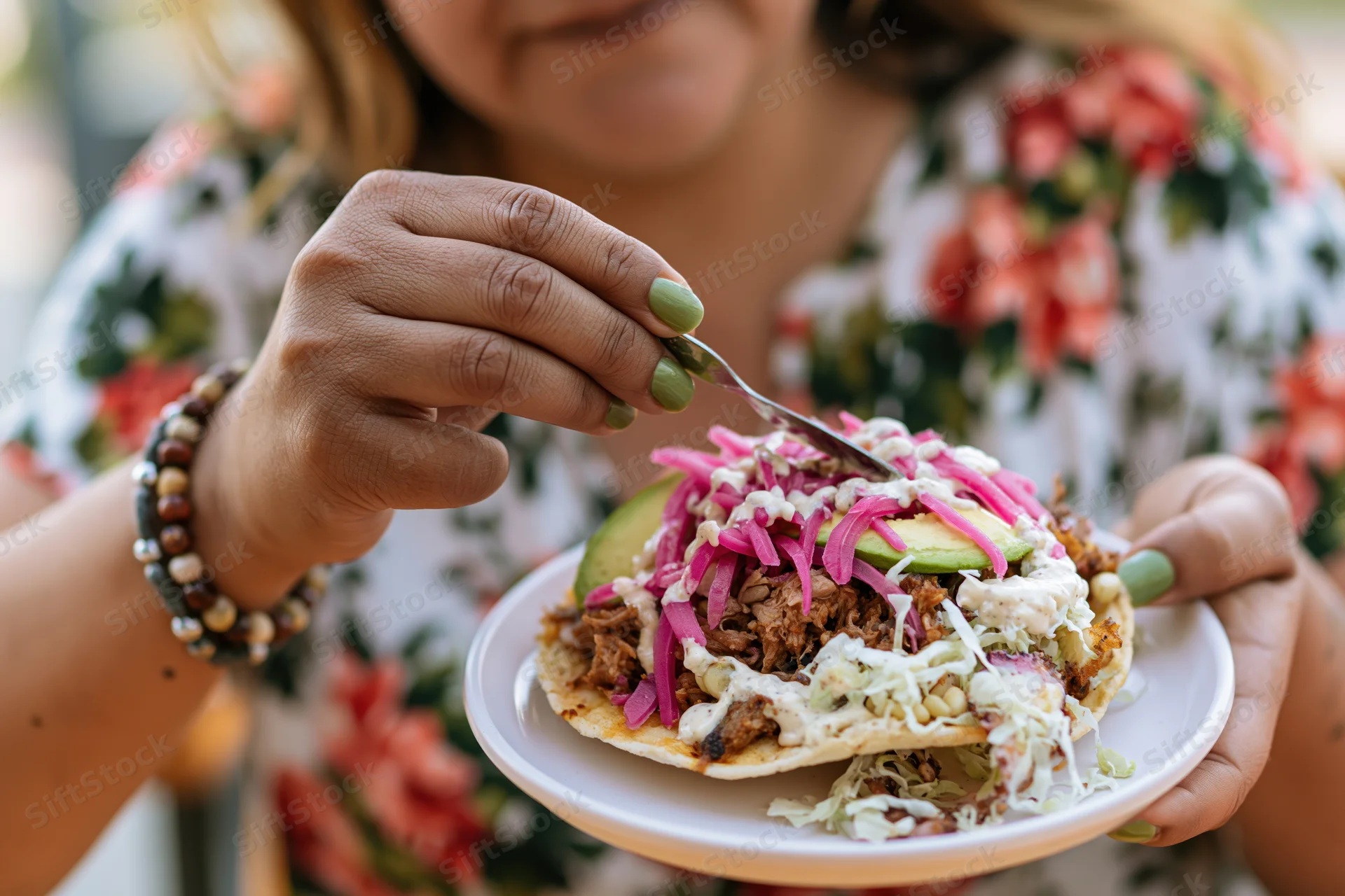 Woman holding a loaded taco with cream sauce, avocado, and pickled onions, eating outdoors