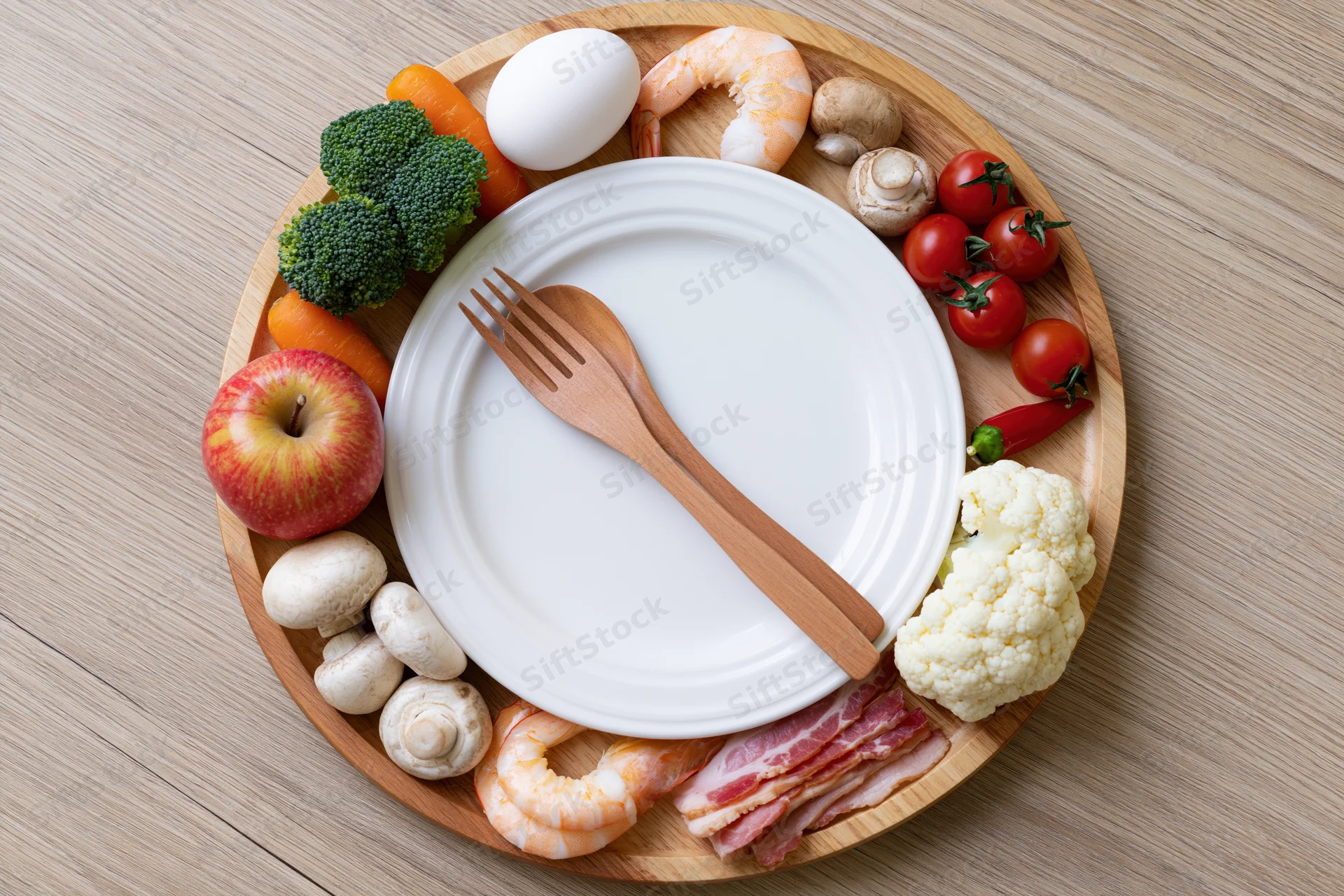 Circular wooden tray with white plate and fork surrounded by various foods arranged like a clock face on a wooden table