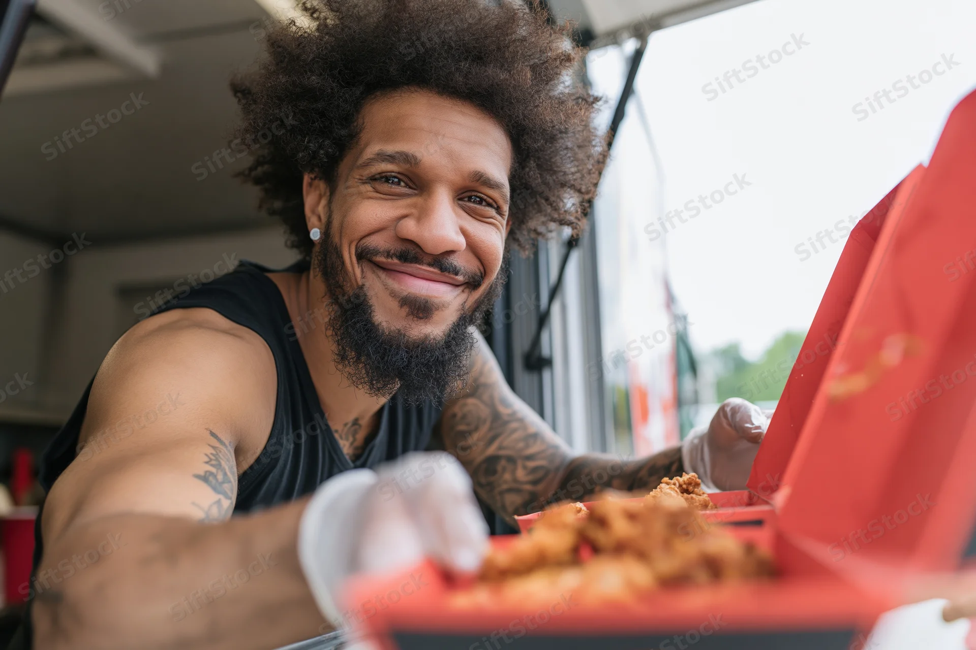 Young black man with afro and tattoos smiling while serving fried chicken from a food truck