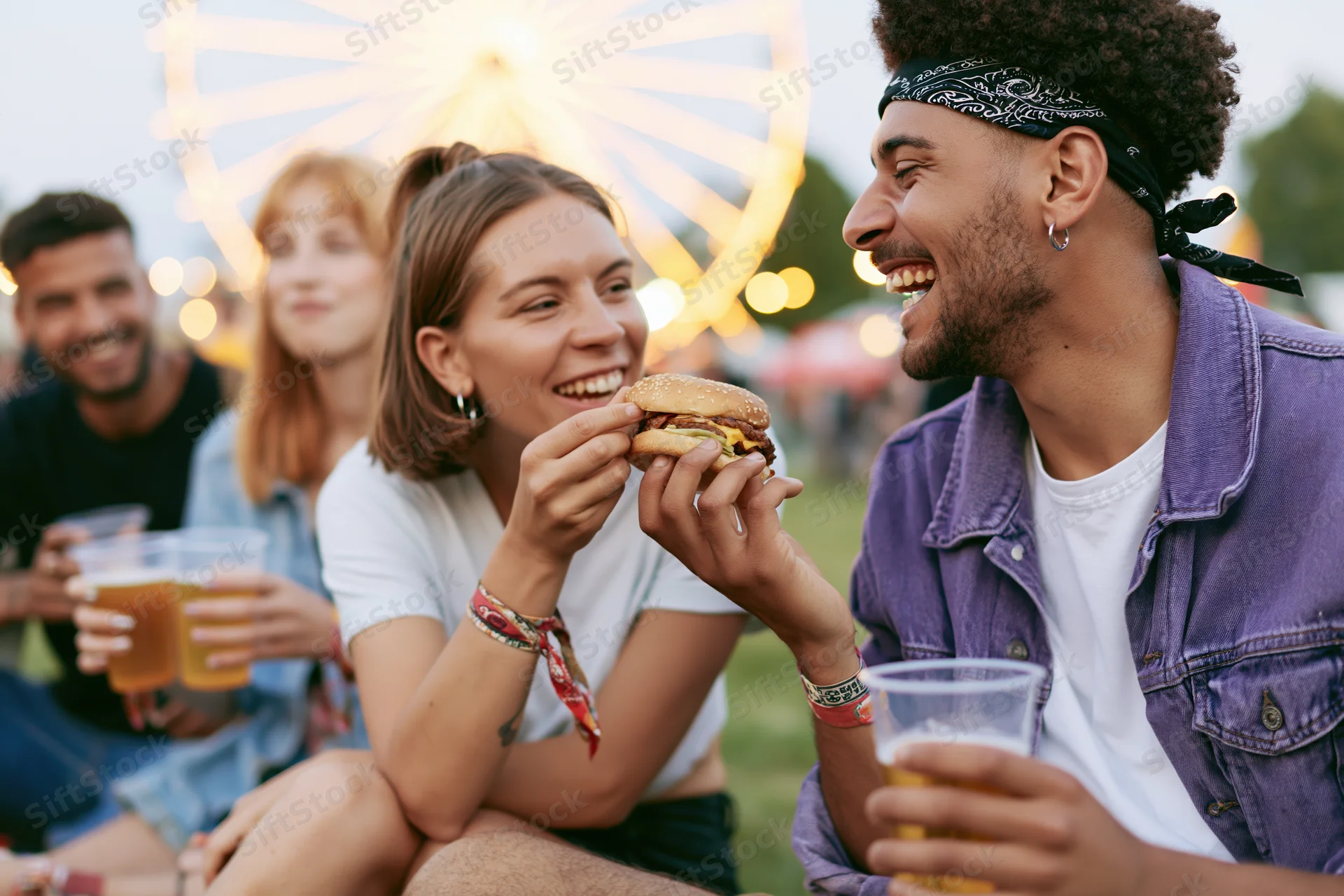 Young woman feeding burger to laughing man at amusement park evening gathering