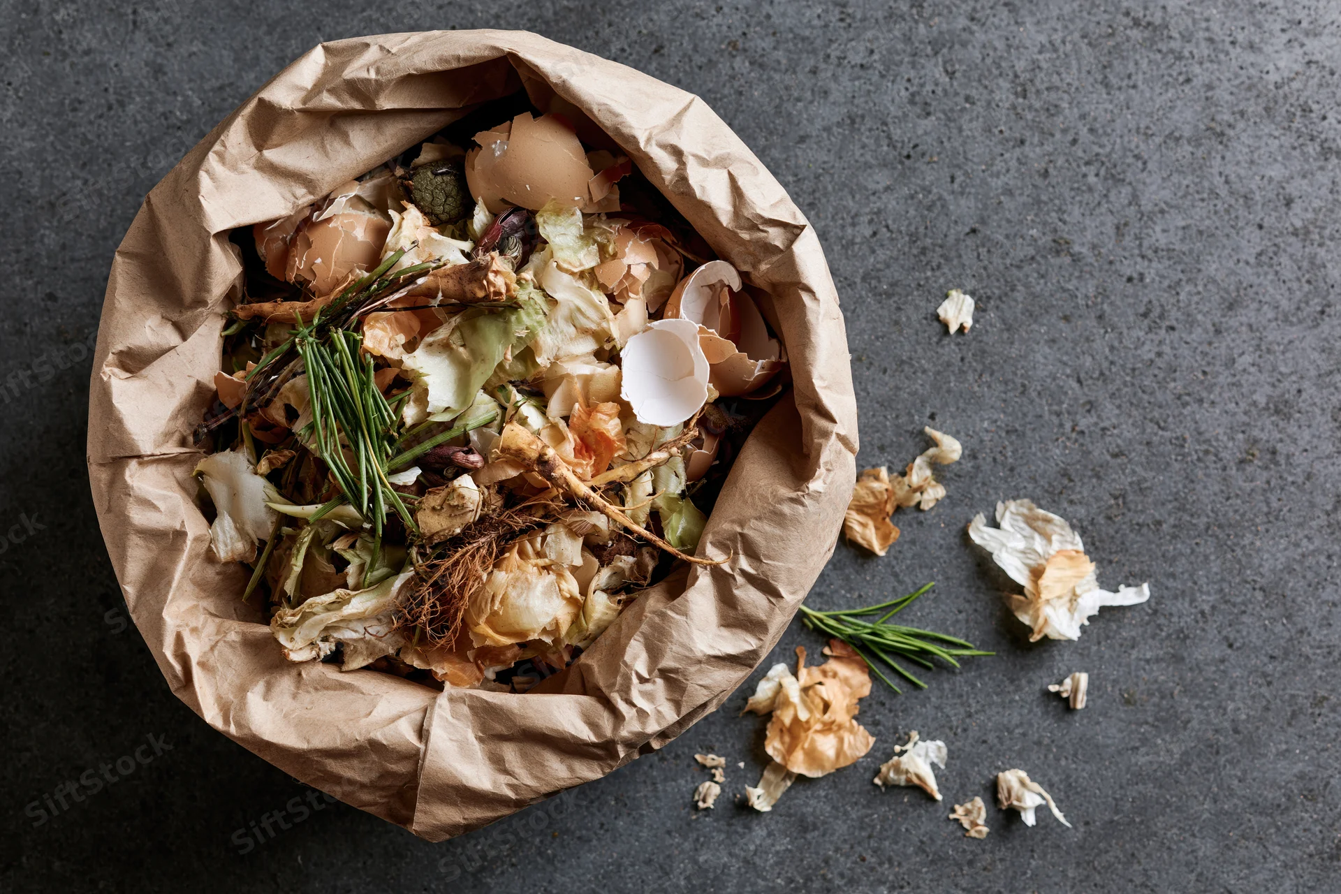 Open brown paper bag filled with kitchen food scraps on dark surface