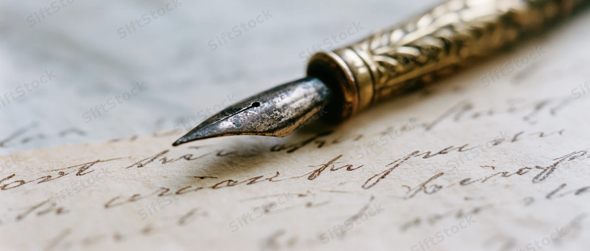 Antique brass pen nib resting on aged yellowed paper with cursive handwriting