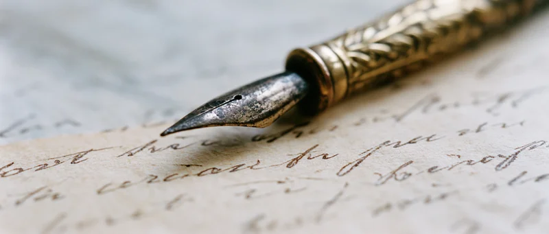 Antique brass pen nib resting on aged yellowed paper with cursive handwriting