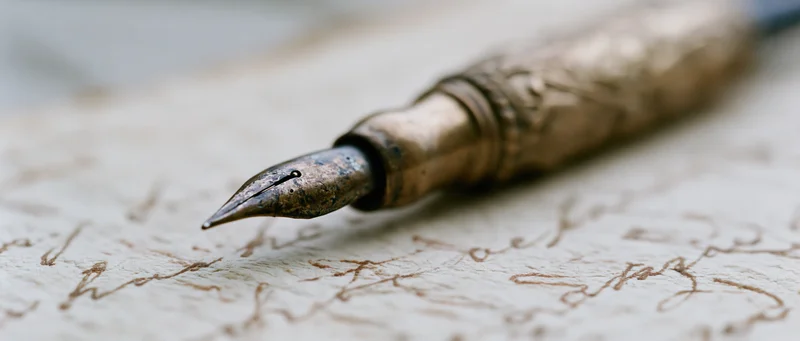 Antique brass fountain pen nib resting on aged yellowed paper with cursive handwriting