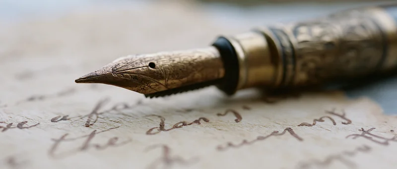 Antique brass fountain pen nib resting on aged yellowed paper with handwritten cursive script