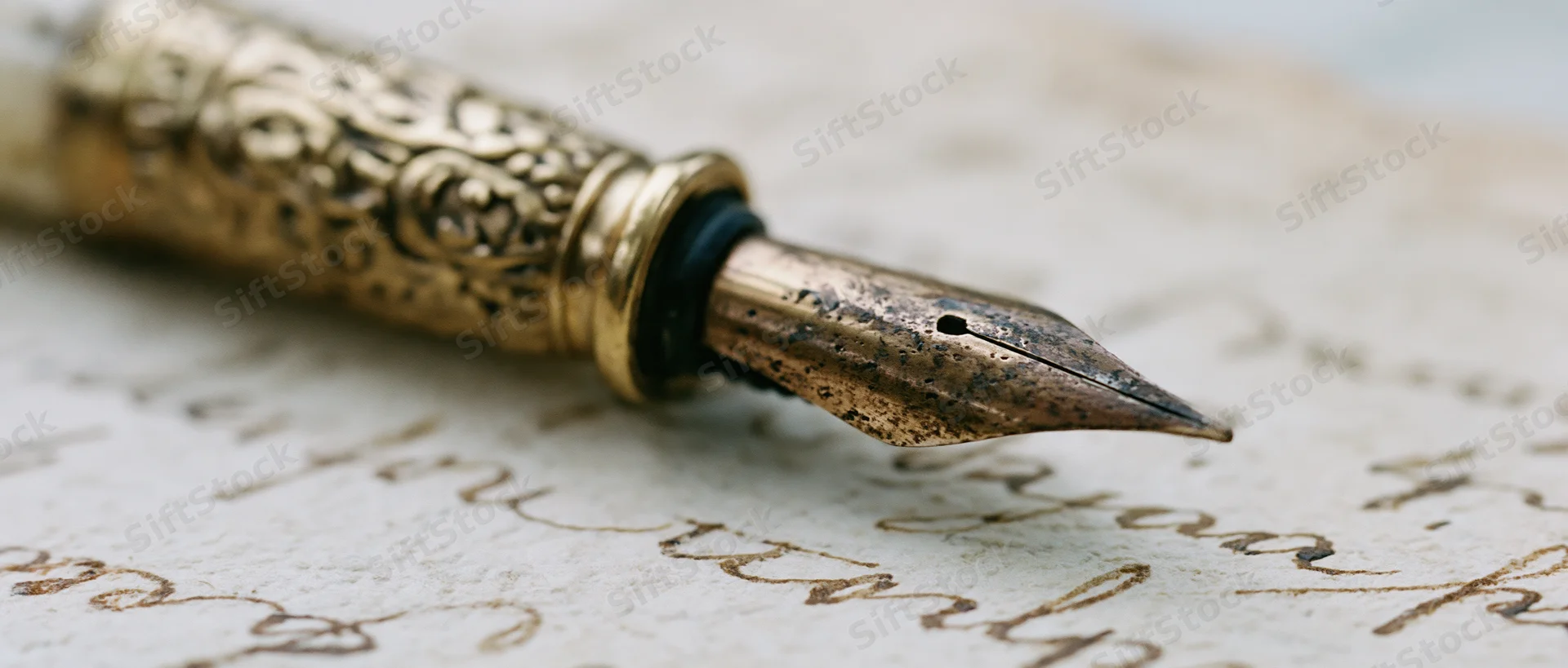 Antique brass fountain pen nib resting on aged yellowed paper with cursive handwriting