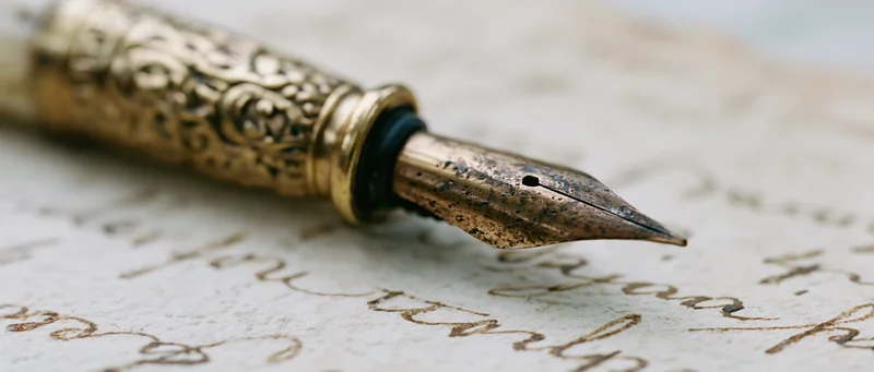 Antique brass fountain pen nib resting on aged yellowed paper with cursive handwriting
