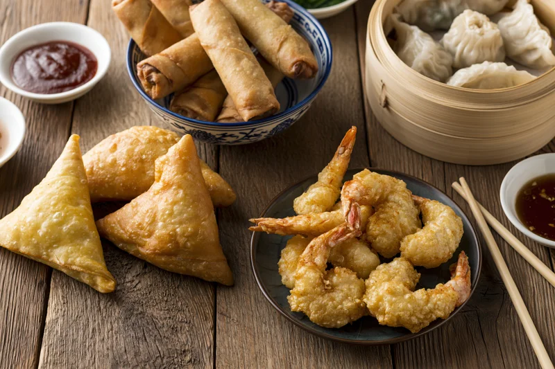Assorted asian appetizers arranged on a rustic wooden table with sauces and chopsticks