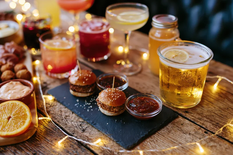 Assorted cocktails and bar snacks arranged on a rustic wooden table with string lights