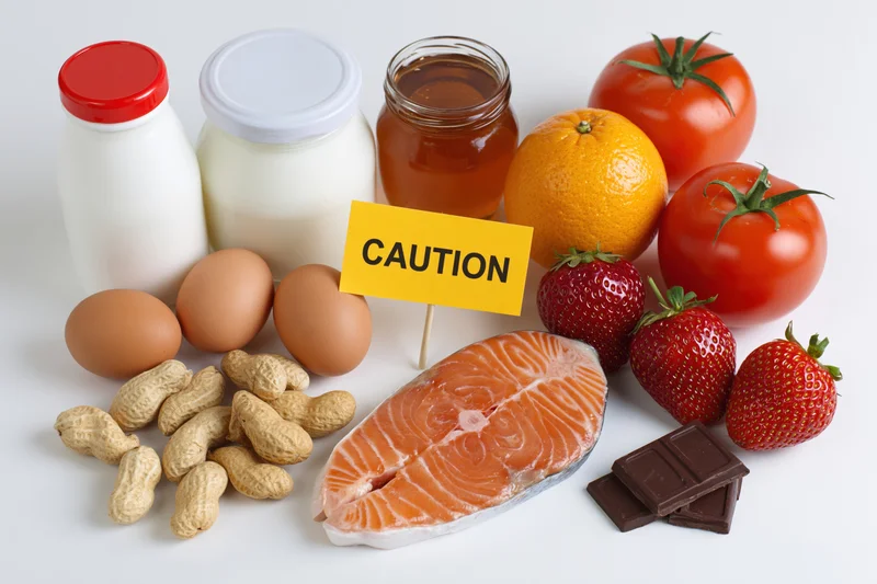 Common food allergens arranged on white surface with caution sign