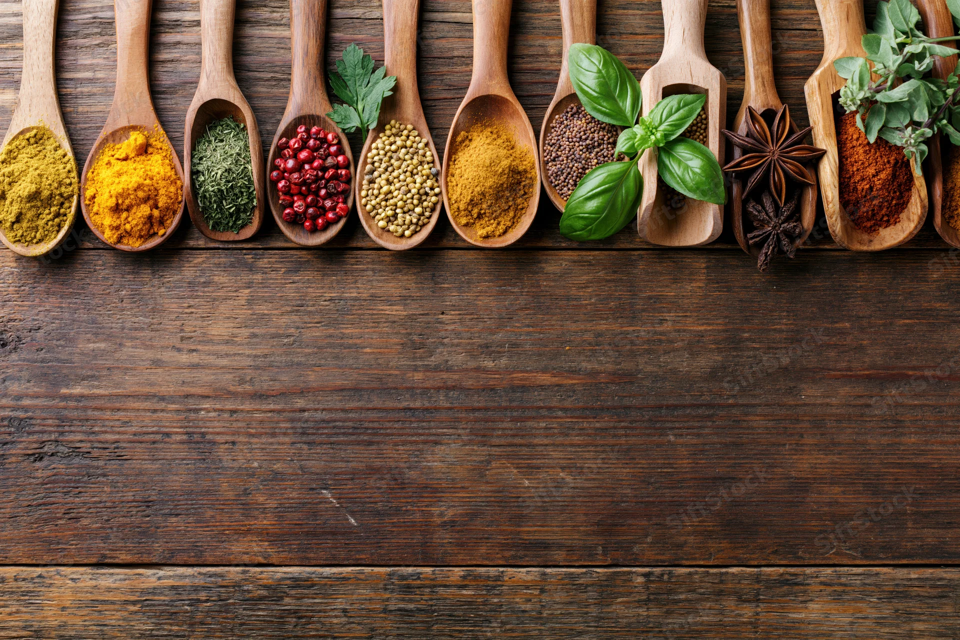 Assorted spices and fresh herbs in wooden spoons arranged on a rustic wooden surface