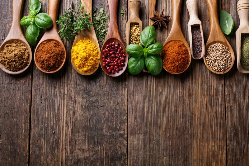Assorted spices and fresh herbs in wooden spoons arranged on dark wood surface