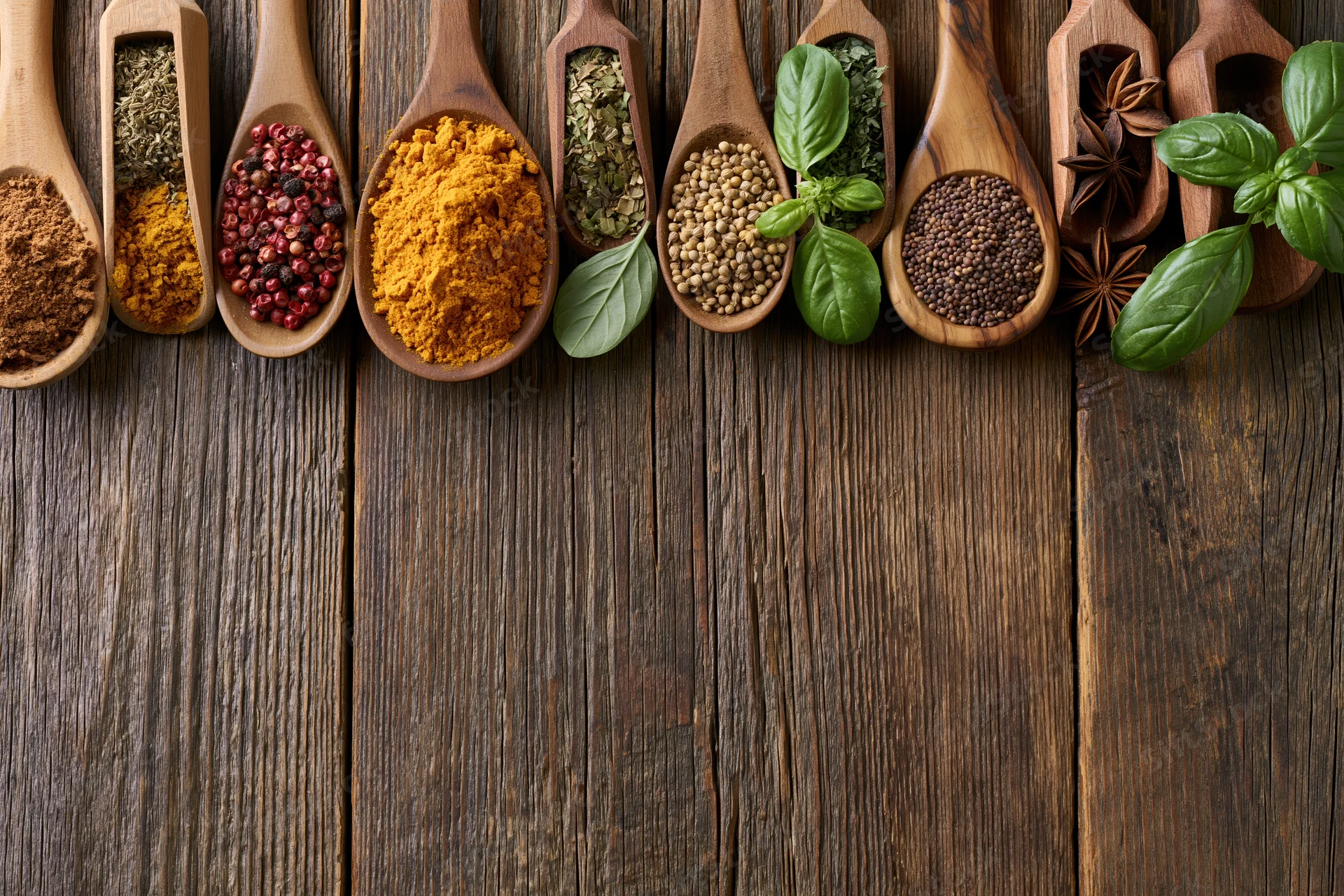 Assorted spices and herbs in wooden spoons arranged on a rustic wooden surface