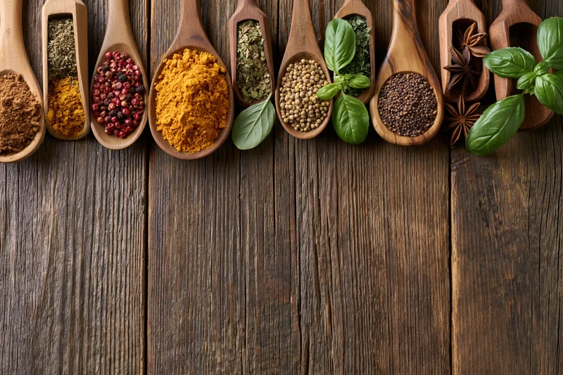 Assorted spices and herbs in wooden spoons arranged on a rustic wooden surface