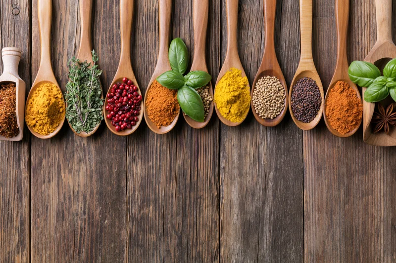 Assorted spices and herbs in wooden spoons arranged on a rustic wooden surface