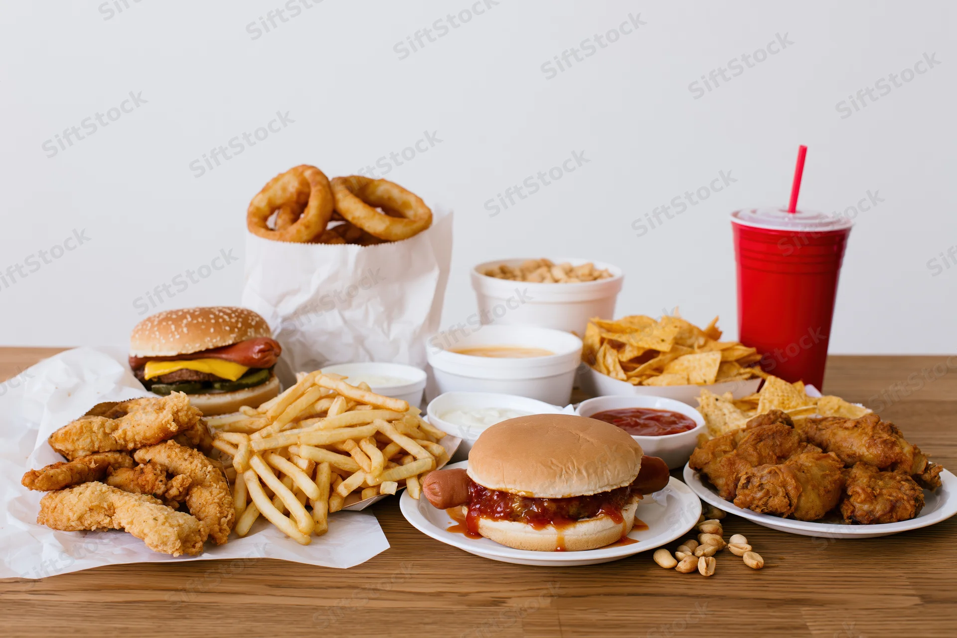 Assorted fast food items including burgers, fries, chicken, and soda arranged on a wooden table