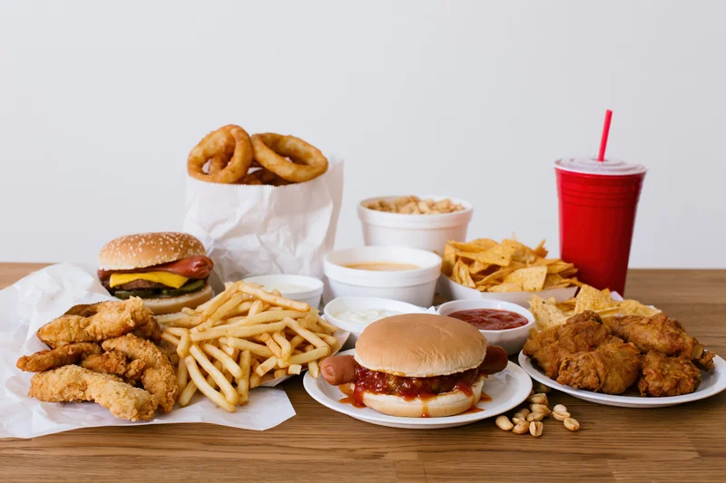 Assorted fast food items including burgers, fries, chicken, and soda arranged on a wooden table