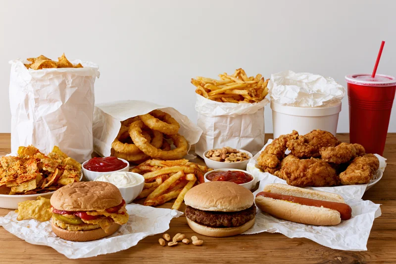 Assorted fast food items including burgers, fries, chicken, and drinks arranged on a wooden table