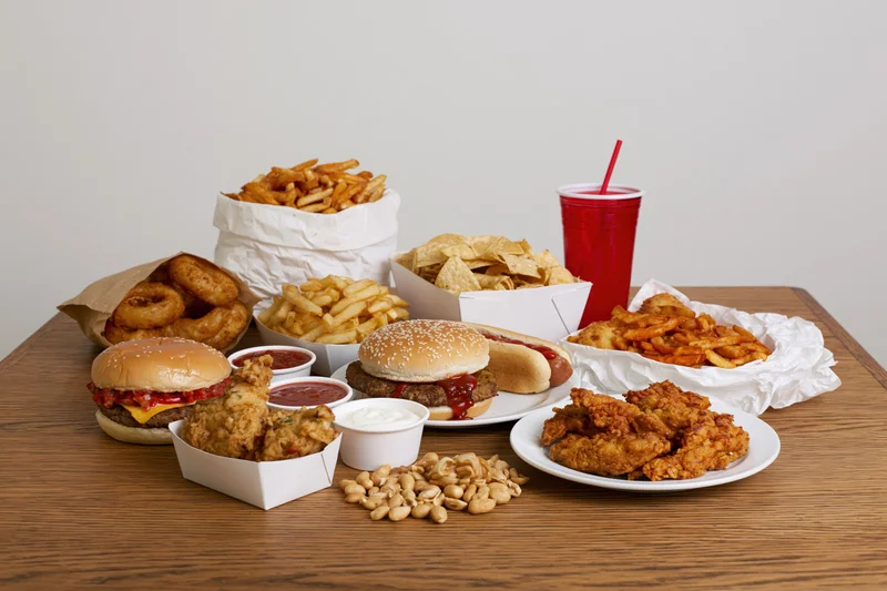 Assorted fast food items including burgers, fries, chicken, and soda arranged on a wooden table