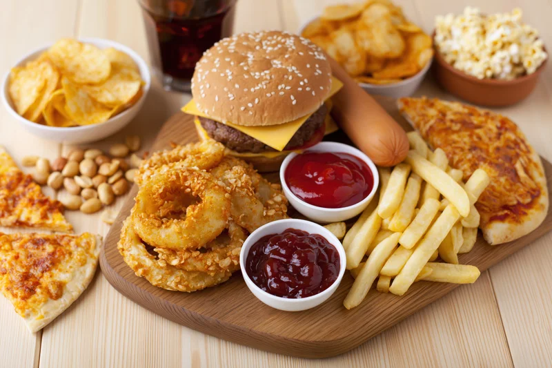Assorted fast food items arranged on a wooden cutting board with condiments and sides