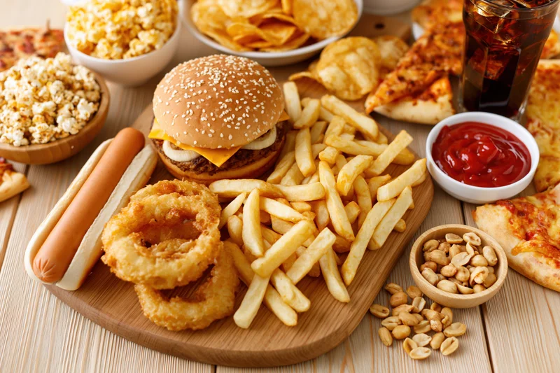 Assorted fast food items arranged on a wooden cutting board with condiments and sides