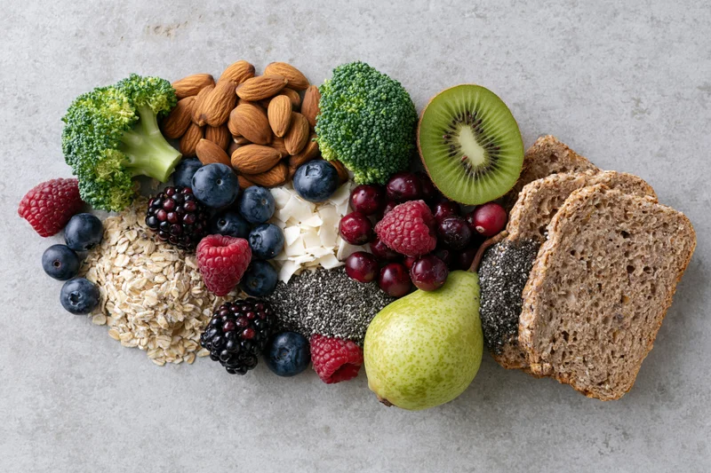 Assorted fresh fruits vegetables nuts seeds and whole grains arranged on a light surface
