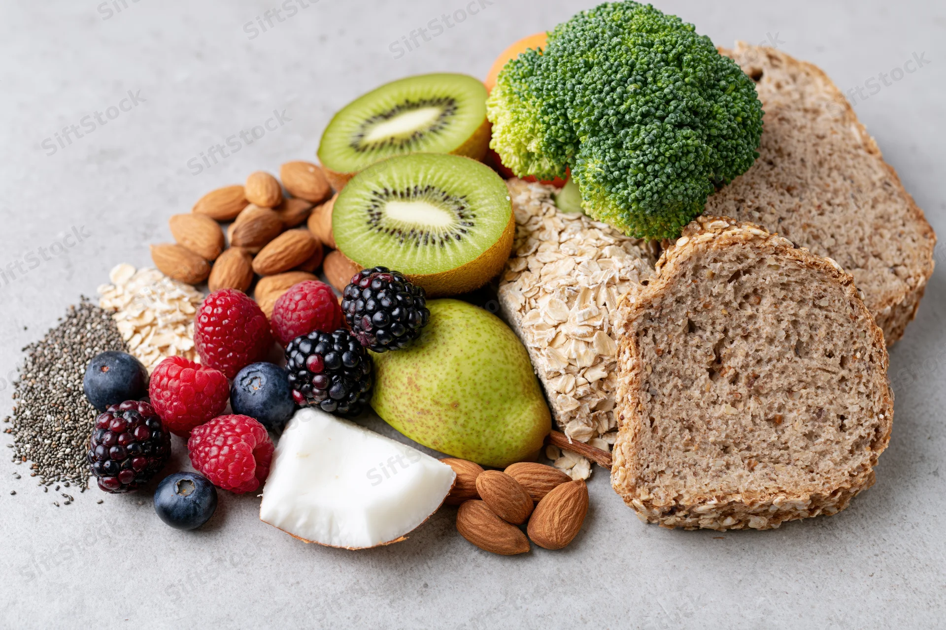 Assorted fresh fruits vegetables nuts seeds and whole grains arranged on a gray surface
