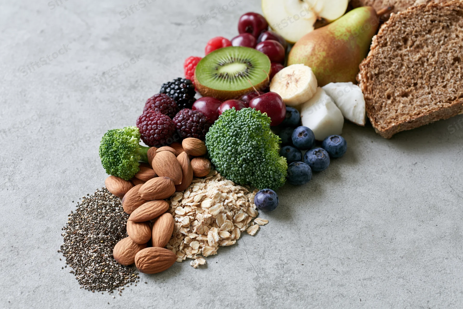 Assorted fresh fruits vegetables nuts seeds and whole grains arranged on a gray countertop