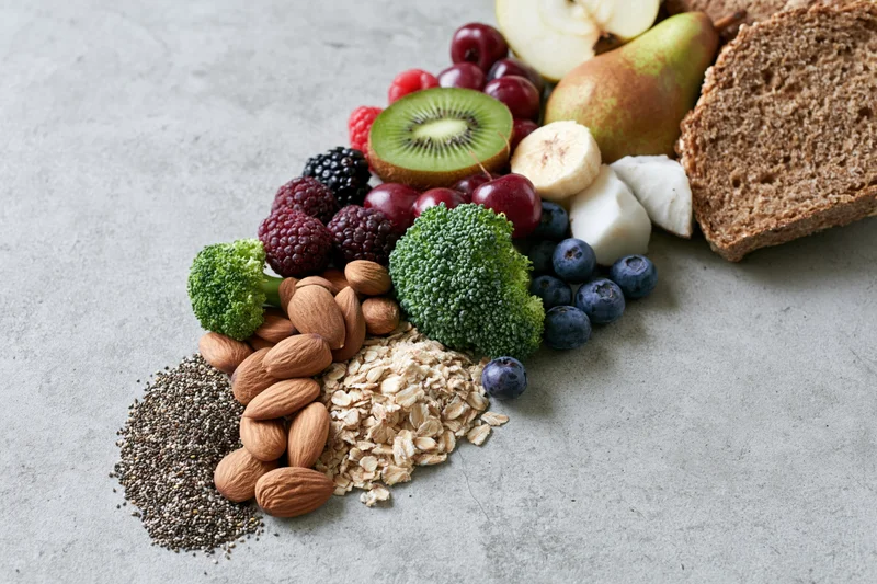 Assorted fresh fruits vegetables nuts seeds and whole grains arranged on a gray countertop