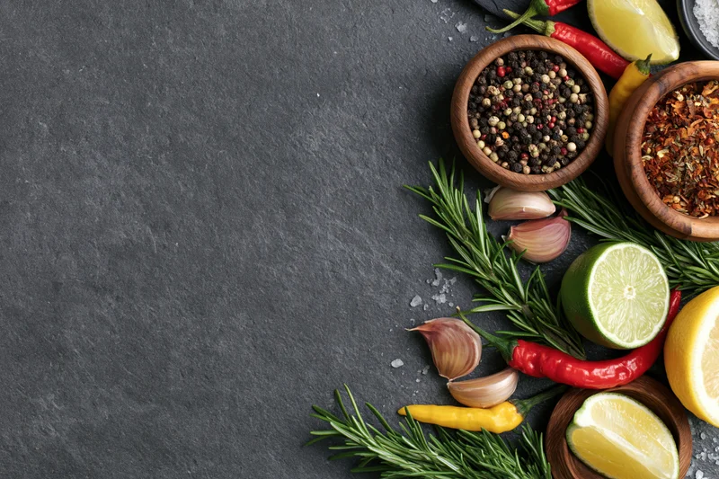 Fresh herbs and spices arranged along the right edge of a dark slate surface