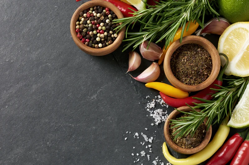 Fresh herbs and spices arranged along the right edge on dark slate surface