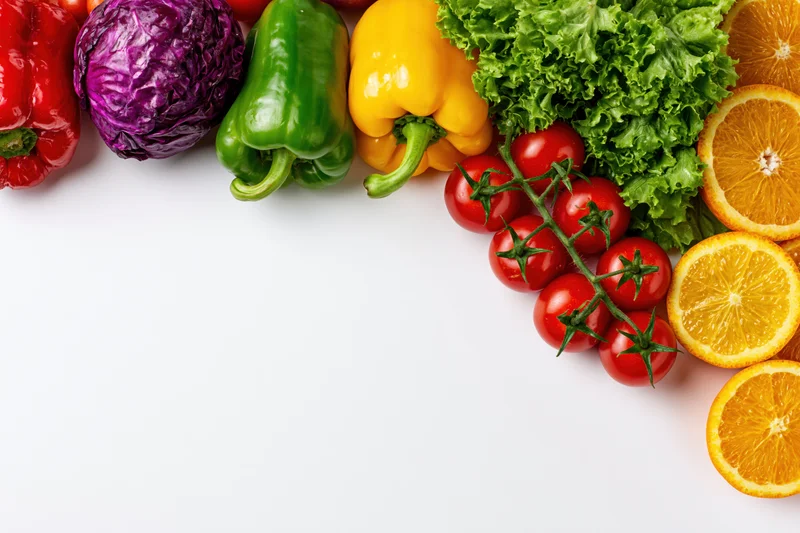 Fresh vegetables and fruits arranged along the top edge on white background