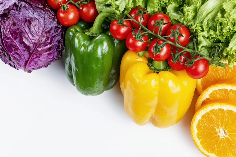 Fresh vegetables and fruits arranged along the top edge on white background