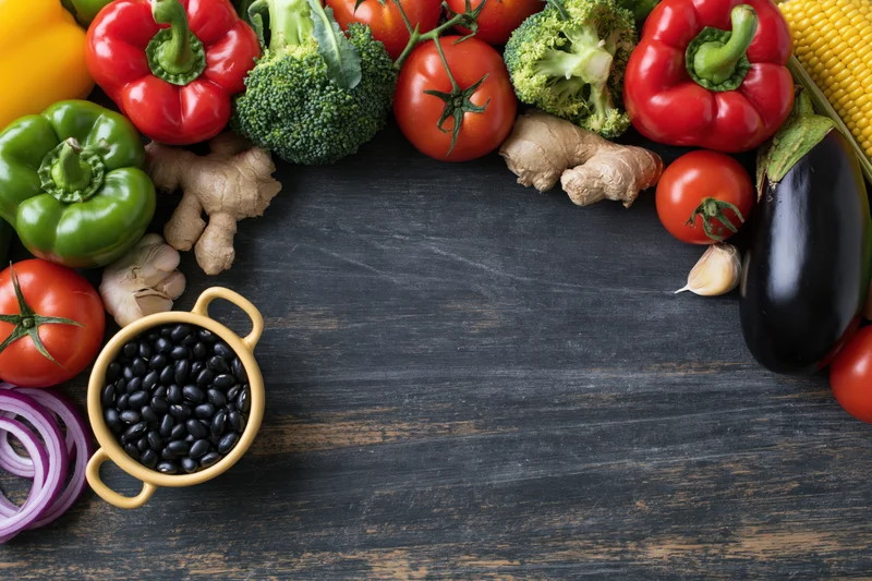 Fresh vegetables and legumes arranged in a border around a dark wooden surface with copyspace in the center