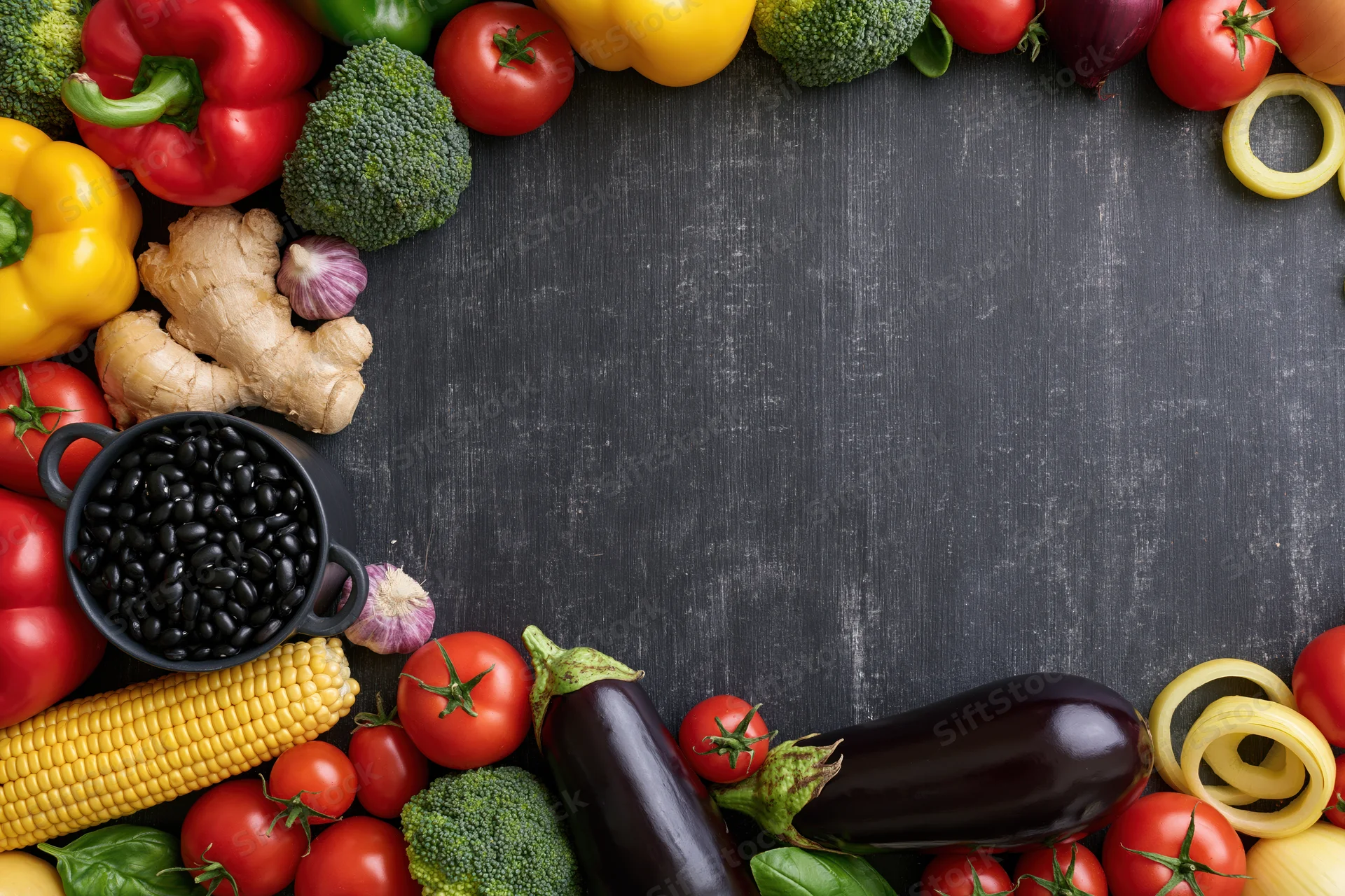 Fresh vegetables and legumes arranged in a border around a dark wooden surface with copyspace in the center