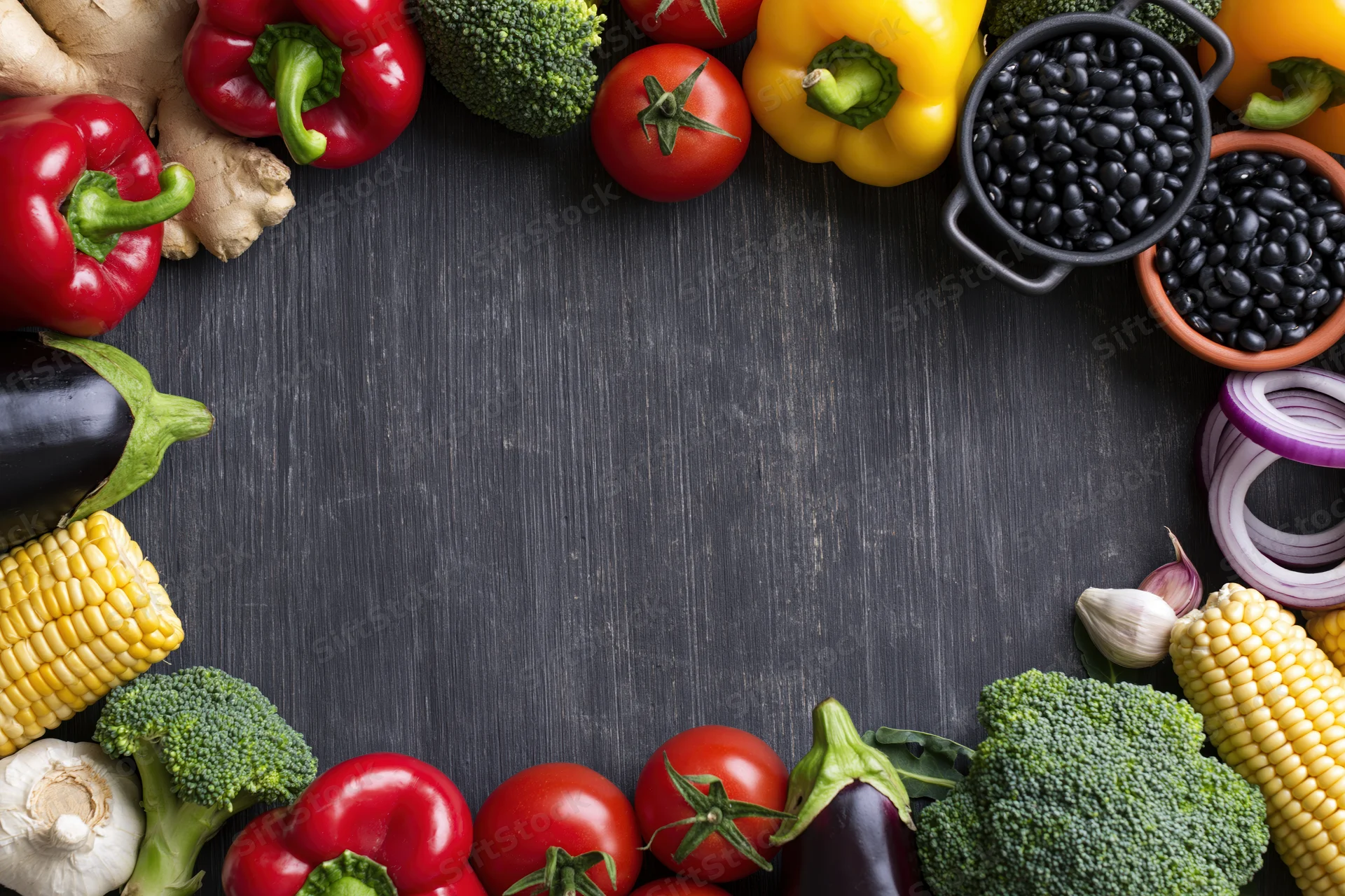 Fresh vegetables and legumes arranged in a border around a dark wooden surface with central copyspace