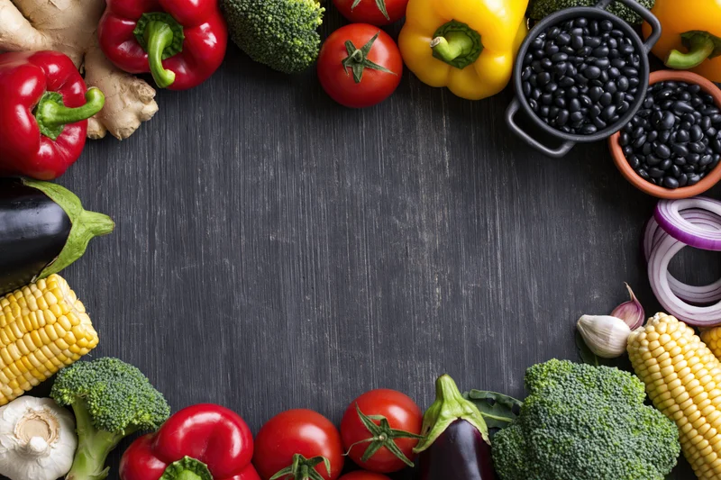 Fresh vegetables and legumes arranged in a border around a dark wooden surface with central copyspace